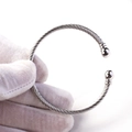 Detail eines gedrehten Silberarmreifs mit polierten Metallperlen, gehalten im weißen Handschuh - Stahlfarbe