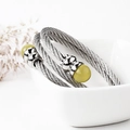 Detail van gedraaide roestvrijstalen kabelarmband met smaragdgroene kralen op wit keramiek - Gele Steen