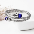 Detailopname van gevlochten zilveren kabelarmband met donkerblauwe stenen op wit keramiek - Blauwe Steen