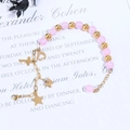 Detalle de cuentas de cristal rosa y dijes dorados con corazón y cruz en la pulsera - Cadena de Oro Cuenta Rosa