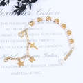 Detalle de pulsera de perlas con colgantes dorados de corazón, cruz, estrella y mariposa - Cadena de Oro Perla Blanca