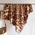 Detail of giraffe print silk scarf draped with a brown leather shoulder bag on a rack - Coffee