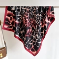 Close-up of silk scarf with giraffe print and red border draped beside a vintage leather bag - Red