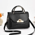 Detail of glossy black crocodile pattern handbag with gold clasp and metal handle - Black