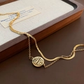 Dubbele gouden titanium stalen enkelband met Fu-hanger op een houten achtergrond - Titanium Stalen Dubbellaagse Enkelband (05-B12) / Goud