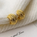 Elegante goldene gedrehte C-Ohrringe präsentiert auf weißem Strickhintergrund - Gold
