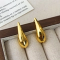 Vista macro de pendientes de gota dorados con acabado de espejo en un joyero de madera elegante - Dorado