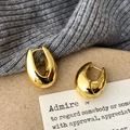 Detail of chunky gold teardrop hoop earrings with high-polish finish on a textured background - Gold
