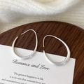 Close-up of matte brushed silver earrings in an irregular teardrop shape on a wooden tray - Large Brushed Style / Silver