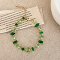 Dettaglio di un bracciale dorato con cristalli verdi irregolari su sfondo in tessuto beige - Oro Zirconia Verde