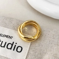 Dettaglio di un anello a tre fasce intrecciate dorate su sfondo in tessuto neutro - Oro