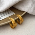 Macro view of layered matte gold C-shaped earrings with brushed texture on ceramic tray - Gold Earrings