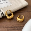 Detail van gouden U-vormige oorbellen met gehamerde textuur op een houten tafelblad - Gouden gehamerde U-vormige oorbellen / Goud