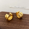 Vista macro de pendientes dorados en forma de C con textura tejida en diagonal - Dorado