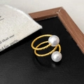 Gedetailleerd beeld van vergulde gevlochten ring met twee witte parels op zwart oppervlak - Meerlaagse Stijl / Goud