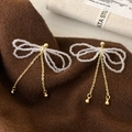 Boucles d'oreilles nœud en cristal et pompons dorés sur fond de tricot chaleureux - Nœud à franges doré