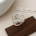 Macro shot of silver wavy double-layer open ring on a dark wooden block with elegant lighting - Silver
