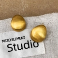 Dettaglio macro di orecchini a goccia in oro spazzolato con texture in metallo opaco - Orecchino a bottone spazzolato color oro