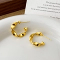 Macro shot of minimalist gold plated twisted hoop earrings on a ceramic dish - Gold