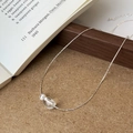 Gros plan d'un collier chaîne argenté avec perle ovale sur un fond en bois rustique - Perle Brossée / Argenté