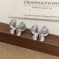 Primer plano de pendientes de mariposa plateados con textura fina sobre base madera - Pendientes de mariposa plateados