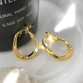Dettaglio di orecchini a cerchio dorati ritorti su piatto in ceramica e candela nera - Forma a goccia intrecciata / Oro