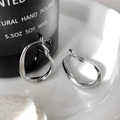 Dettaglio di orecchini a cerchio ondulati argento su uno sfondo estetico e minimalista - Ondulato Irregolare / Argento