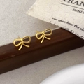 Macro shot of polished gold bow stud earrings on a dark wood and fabric background - 3D Twisted Bowknot (A-1428)