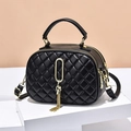 Black quilted crossbody bag with golden ring tassel charm on a display stand - Black