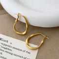 Detail of matte gold oval hoop earrings with a twisted design on white ceramic and card - Matte Gold Hoop Earrings