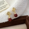 Detail van gouden vlinder oorbellen met kattenoogstenen en rode parels op een tray - Rood