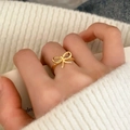 Nahaufnahme eines eleganten Goldrings mit Schleife am Finger und Strickpullover - Goldener Schleifenstil (C-391)