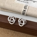 Detail of interlocking silver knot earrings showing polished texture on a wood surface - Triple Ring Intertwined Mobius Studs (A-1430) / Silver