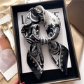 Elegant paisley and polka dot printed silk scarf tied in a bow on a luxury magazine - Black