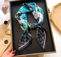 Detail of checkered square silk scarf with floral print and monogram pattern on a display tray - Blue