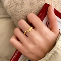 Elegante gouden golfring met minimalistisch ontwerp gedragen op hand bij rood boek decor - Goud Golfstijl (C-272)