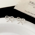 Macro shot of minimalist silver bow earrings with polished finish on a porcelain tray - Fine Line 3D Bowknot Style (A-1428)