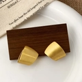 Detailed close-up of geometric brushed gold earrings on a rustic wood block - Irregular Geometric Trapezoid Style (A-1576)