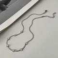 Dettaglio dei ciondoli a cuore d'argento su una catena piatta su superficie bianca - Argento