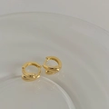 Dettaglio di orecchini huggie placcati in oro con linee intrecciate e finitura lucida - Oro