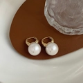 Detailweergave van elegante gouden parel hoops op een bruin lederen display - Goud met grote parel