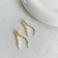 Detail of gold-plated tassel earrings with white pearls on a textured white surface - Pearl Gold Bead Earrings