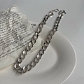 Close-up of a silver curb chain necklace featuring an OT buckle over a white ceramic plate - Silver Color Gold Plated