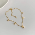 Detail eines minimalistischen Gold-Fußkettchens mit mehreren Kugeln an einer feinen Kette - Gold