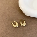 Detail van vergulde hoefijzervormige oorbellen op een minimalistische bruine achtergrond - Gouden U-vormige oorbellen