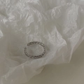 Dettaglio di un anello regolabile a catena d'argento su sfondo di carta bianca testurizzata - Stile Vuoto Sottile / Argento