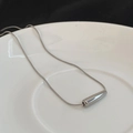 Detalle del colgante de gota plateado y cadena de serpiente en un plato de cerámica - Plateado
