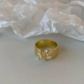 Close-up of golden open ring featuring asymmetrical zircon stone clusters on a textured surface - Gold