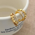 Dettaglio di tre orecchini dorati con zirconi incastonati sul bordo di una tazza di ceramica - Oro