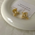 Detailed macro view of S925 hallmark on gold twisted sculpture earrings on white ceramic - Gold